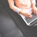 Kobieta trzymająca laptopa na kolanach i pisząca posta na swój blog hotelarski